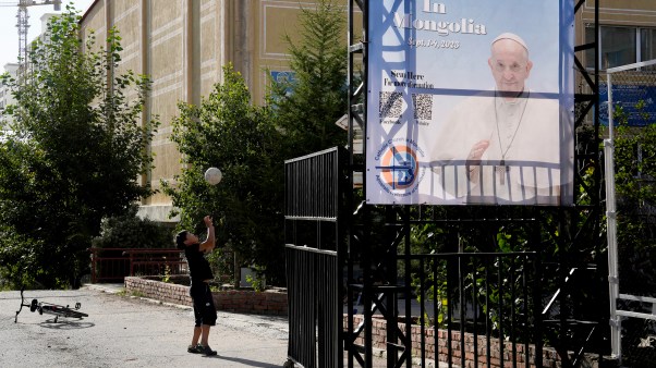 A Mongolian child plays with a ball near a banner promoting the visit of Pope Francis in Ulaanbaatar, Mongolia.