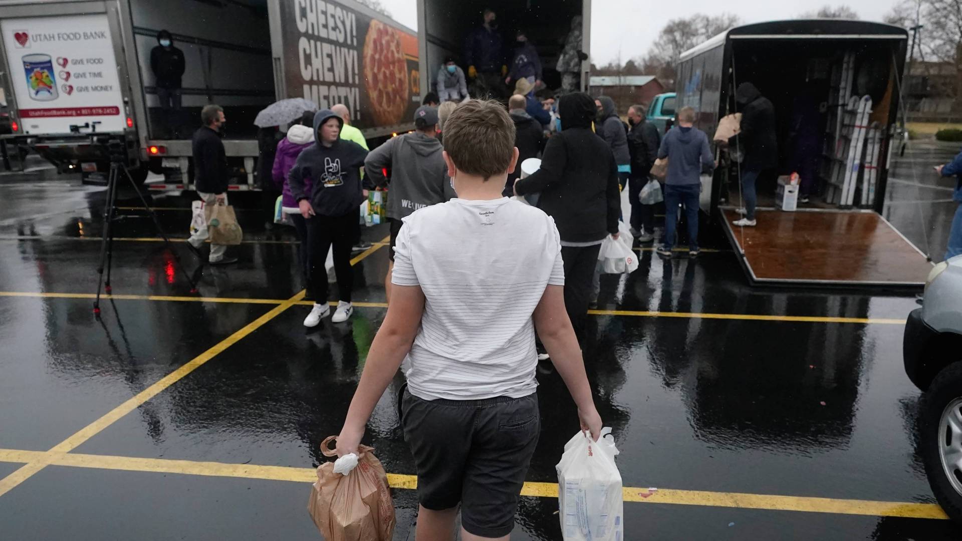 Boy carries plastic bags of food to a row of trucks at collection site.