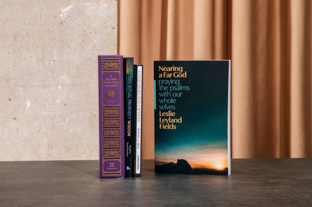 Photograph of "nearing a far God" book next to a stack of books against a half concrete wall half orange curtain