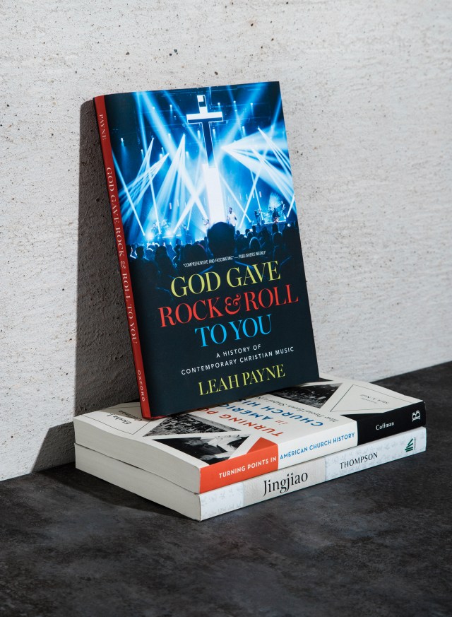 Photograph of "God rock and roll to you" book on a stack of books leaning against a concrete wall