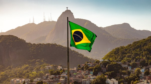 Brazilian flag flying over a town called Corcovado with mountains in the background with the Christ the Redeemer statue on top.