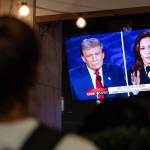 Person watches debate on a TV screen depicting Trump and Harris side by side with a flag beside it.