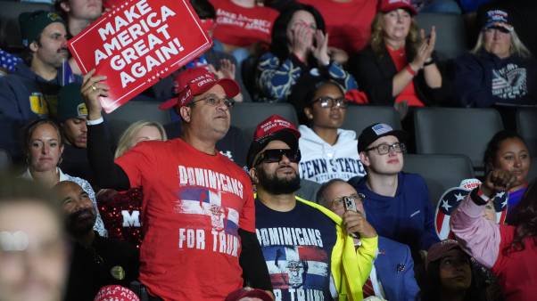 Men hold MAGA signs and wear "Dominicans for Trump" signs at a rally in Allentown, Pennsylvania.