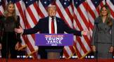 Donald Trump gives victory speech on stage with American flags behind him.