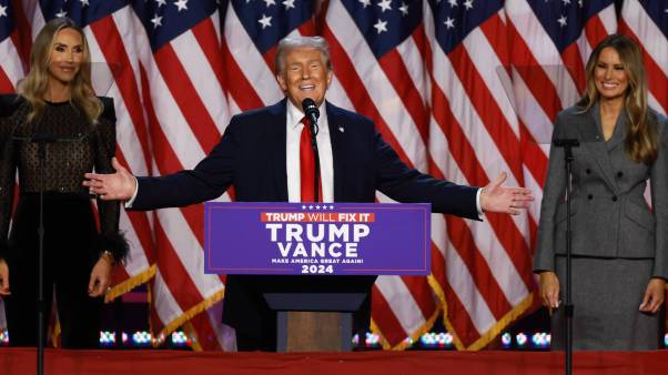 Donald Trump gives victory speech on stage with American flags behind him.