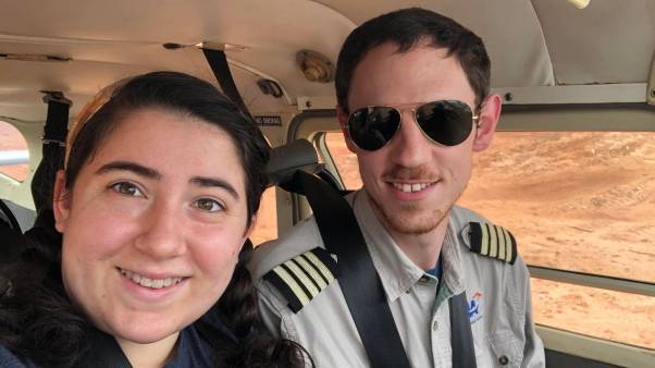 A woman poses for a selfie with a man wearing a pilot's uniform and aviator sunglasses.