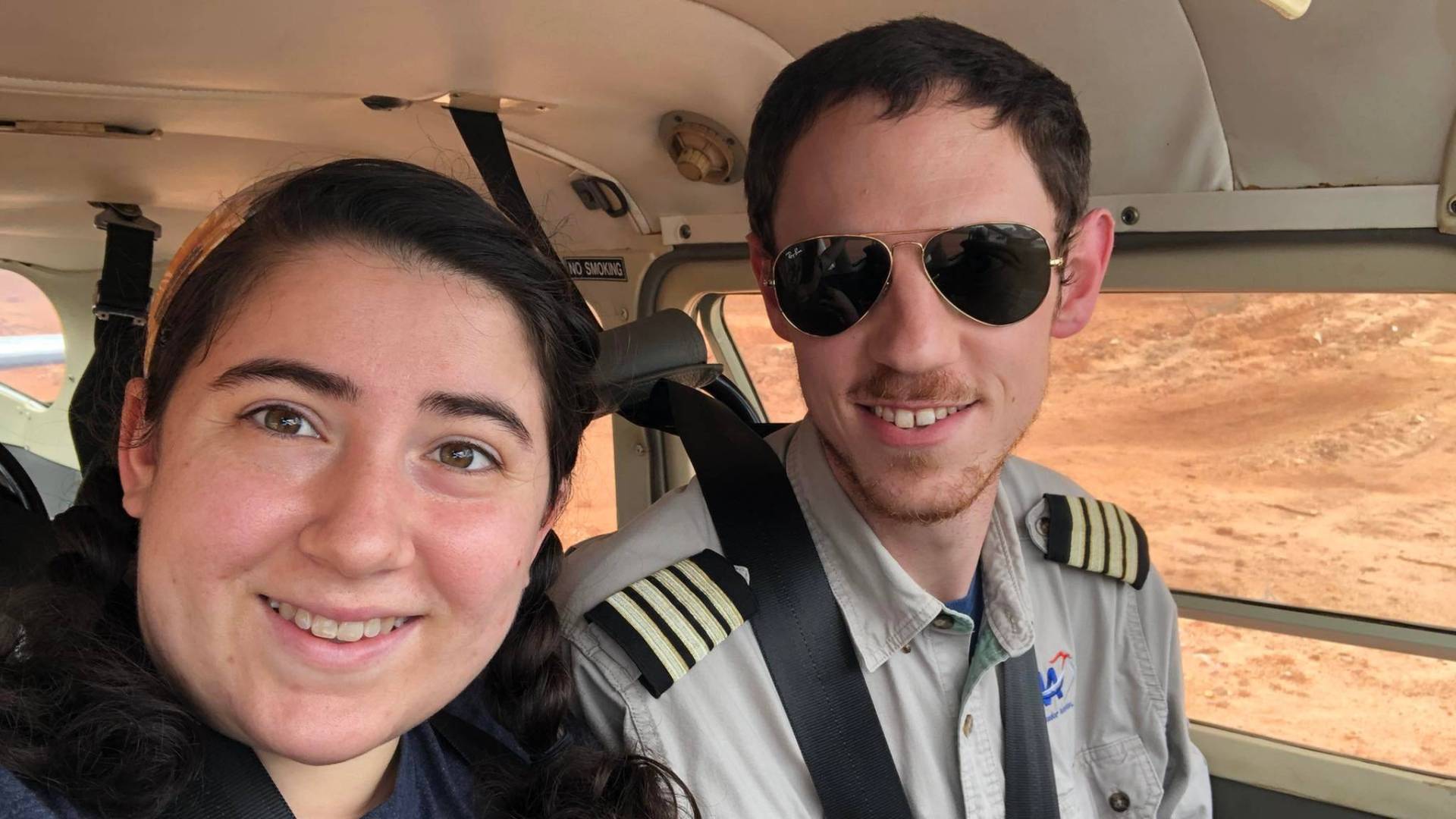 A woman poses for a selfie with a man wearing a pilot's uniform and aviator sunglasses.