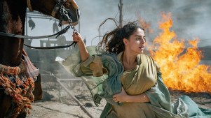 Mary holding onto a horse with a fire behind her.