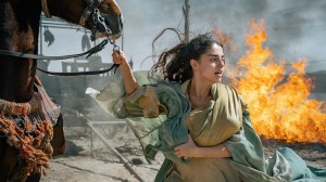 Mary holding onto a horse with a fire behind her.