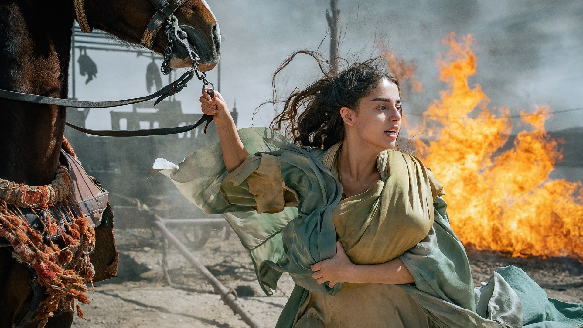 Mary holding onto a horse with a fire behind her.