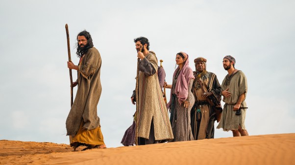 Wasim No’mani as Moses holding a staff in the desert with Israelites walking behind him