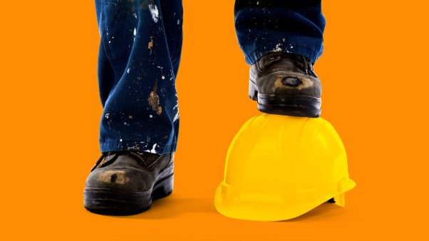 A construction workers dirty jeans and boots with one boot standing on a yellow construction hat