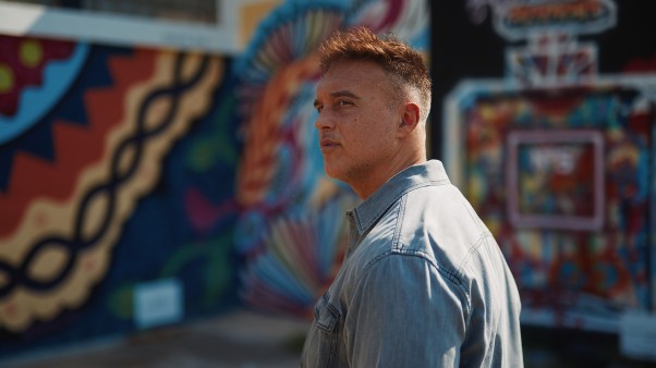 Portrait of Joshua Broome standing against a graffitied wall