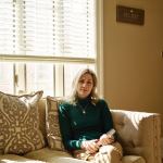 A photo of Jennifer Nizza on a couch with a book in her hand