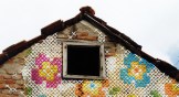 An old brick house with cross stitched flowers over it.